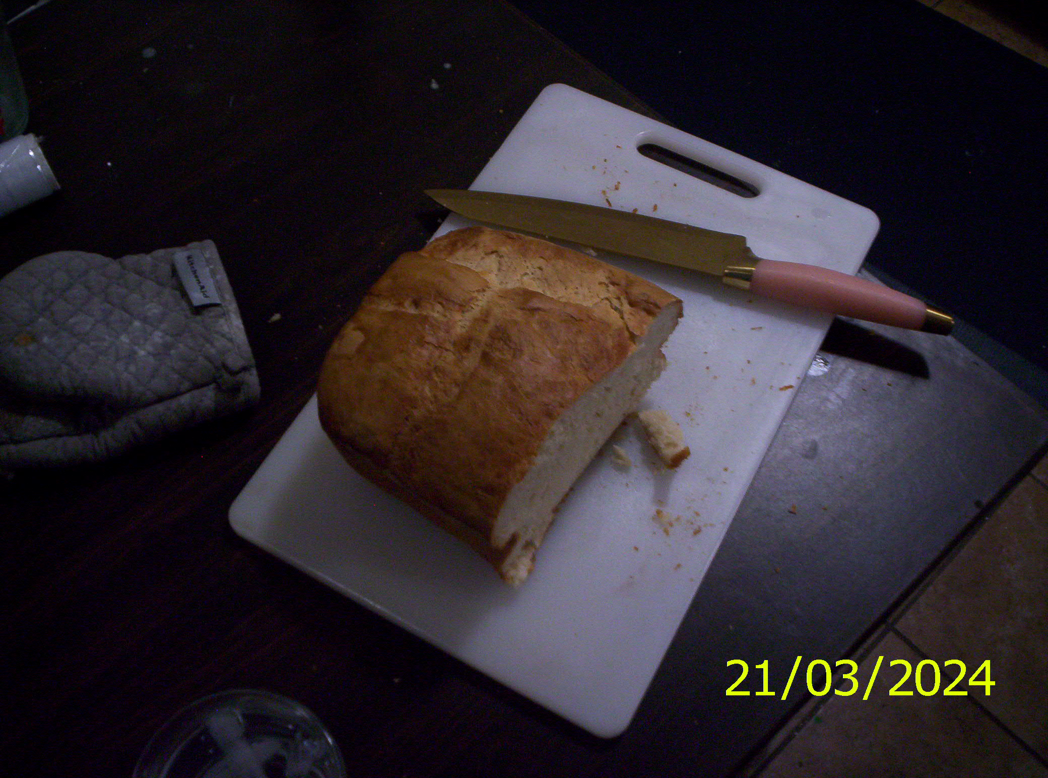 White bread on a cutting board, the top of the bread is oversized. The bread has had some of it cut off already.